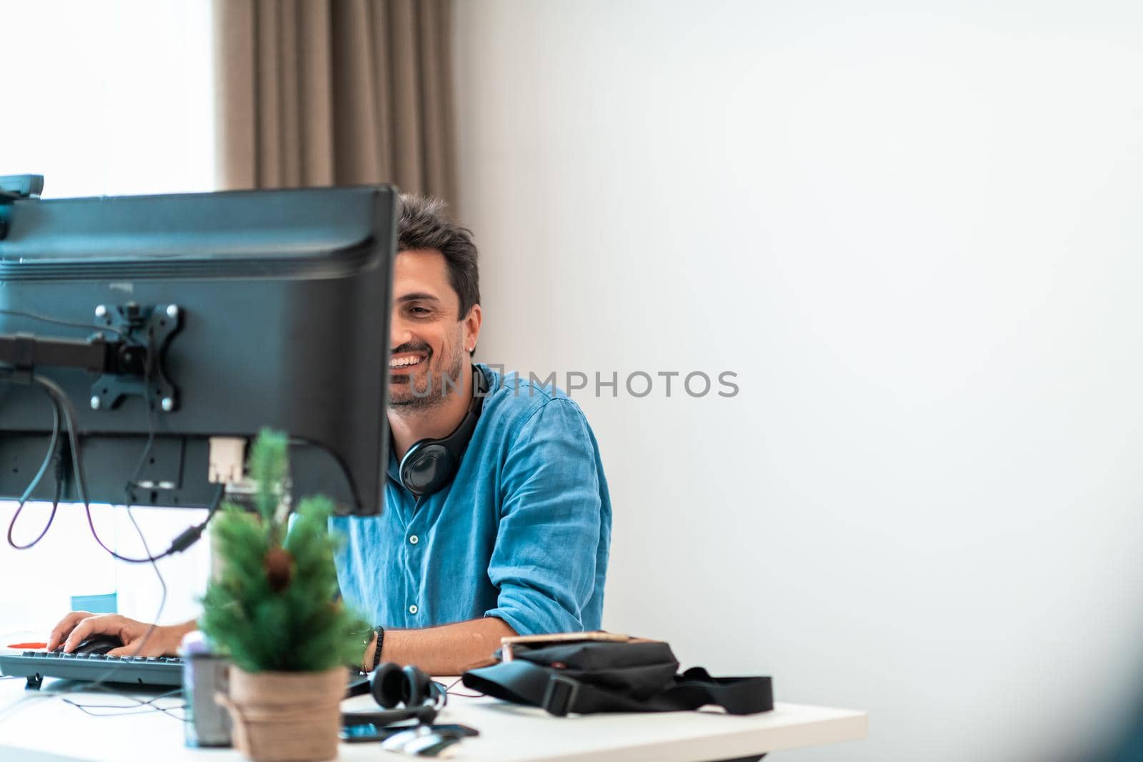 Casual man working on desktop computer in modern open plan startup office interior. Selective focus by dotshock