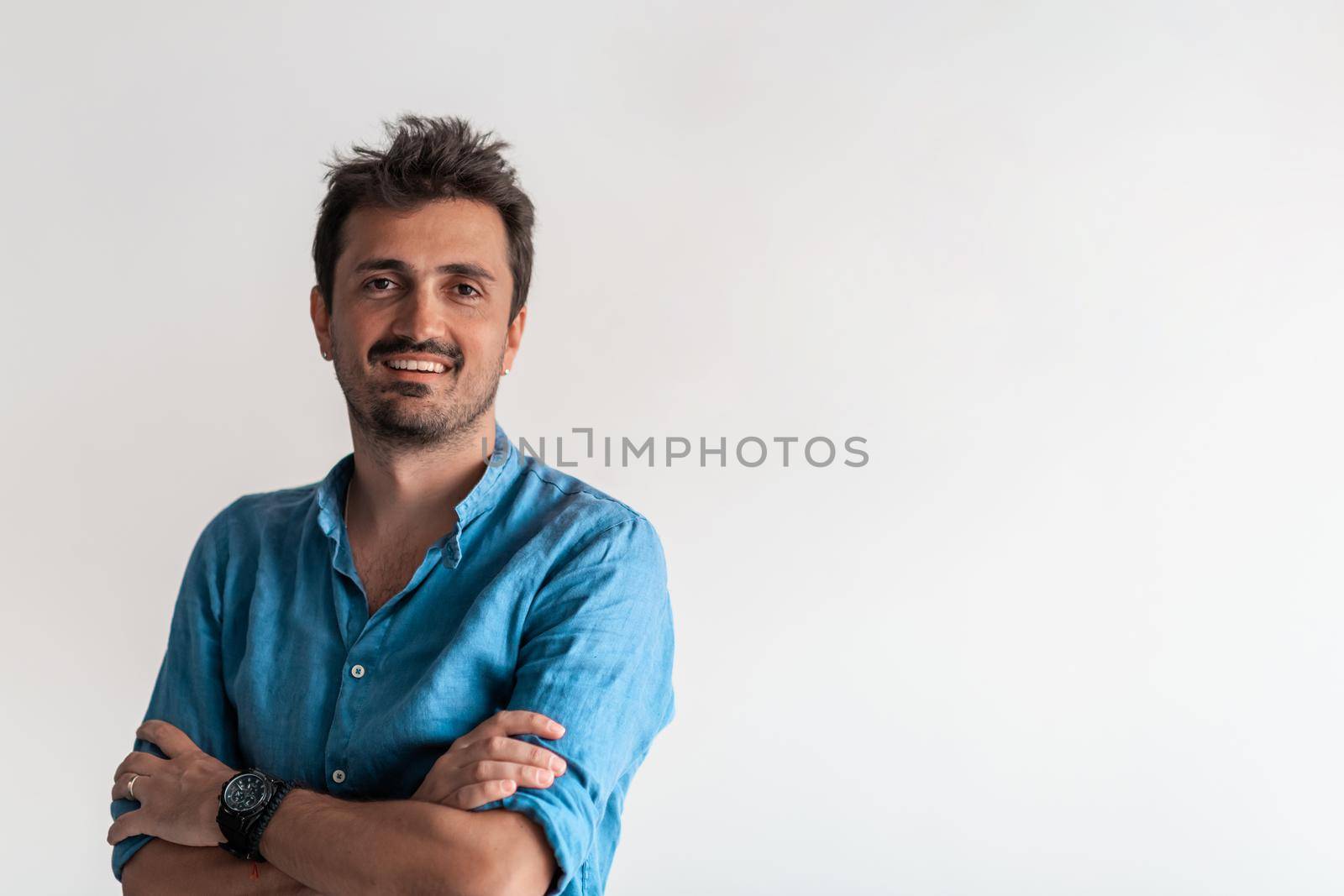 Formal business male portrait. A confident successful casual businessman or manager stands in front of a white background, arms crossed, looking directly at the camera and smiling friendly. High-quality photography.