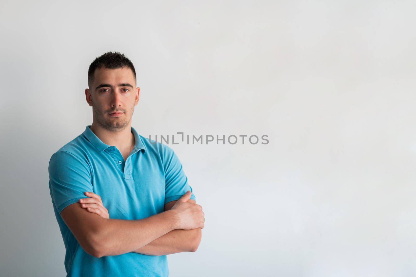 Formal business male portrait. A confident successful casual businessman or manager stands in front of a white background, arms crossed, looking directly at the camera and smiling friendly. High-quality photography.