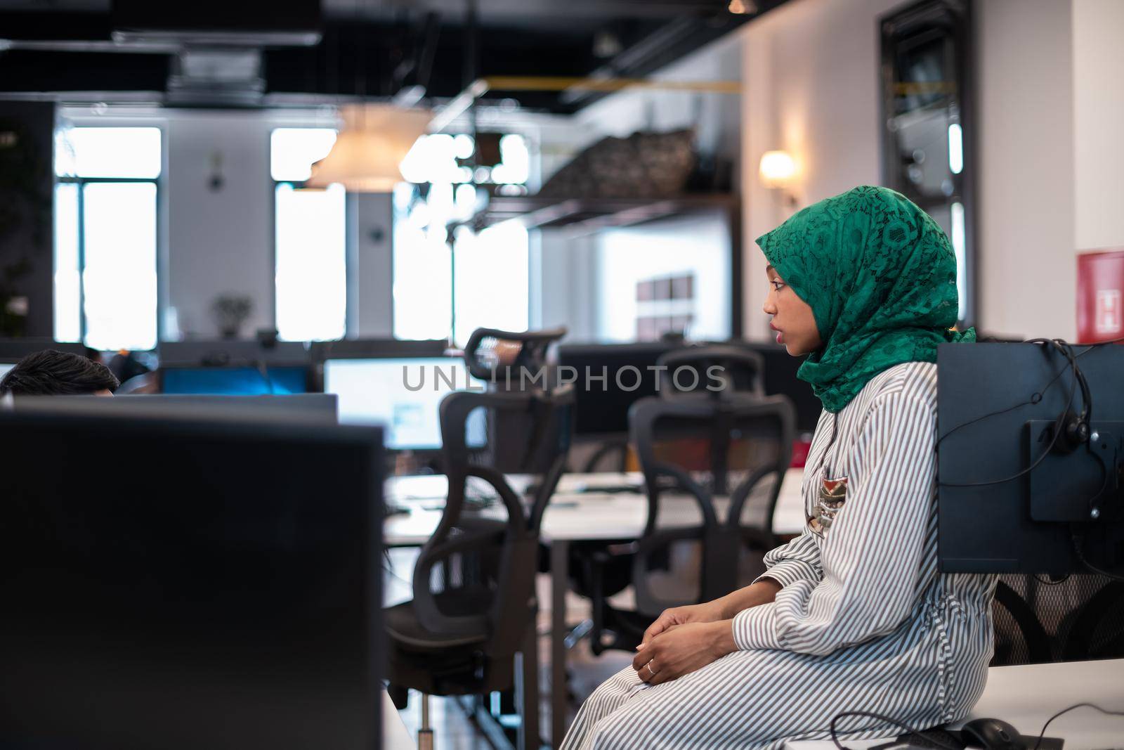 Arabian woman wearing a hijab on meeting in modern open plan office interior brainstorming, working on laptop and desktop computer. Selective focus. High-quality photo