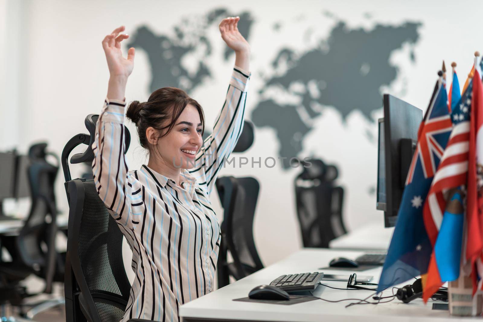 Happy casual businesswoman celebrating success while working on a desktop computer in a modern open plan startup office interior. High-quality photo