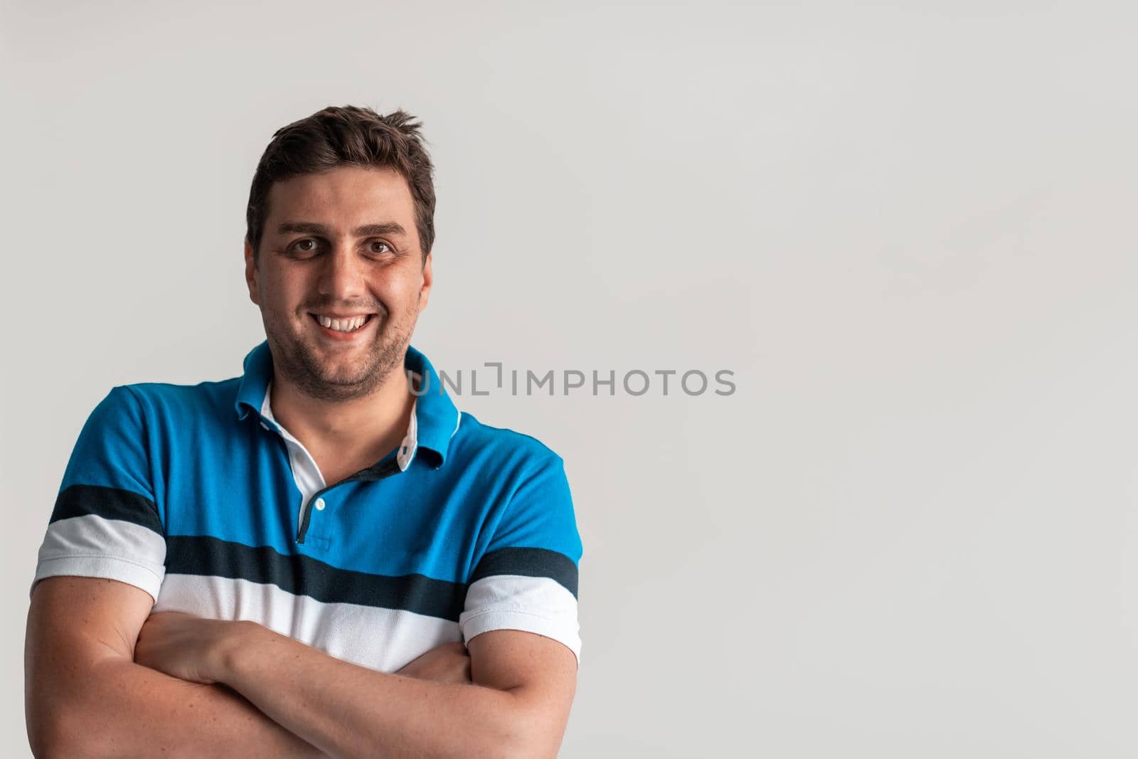 Formal business male portrait. A confident successful casual businessman or manager stands in front of a white background, arms crossed, looking directly at the camera and smiling friendly. High-quality photography.