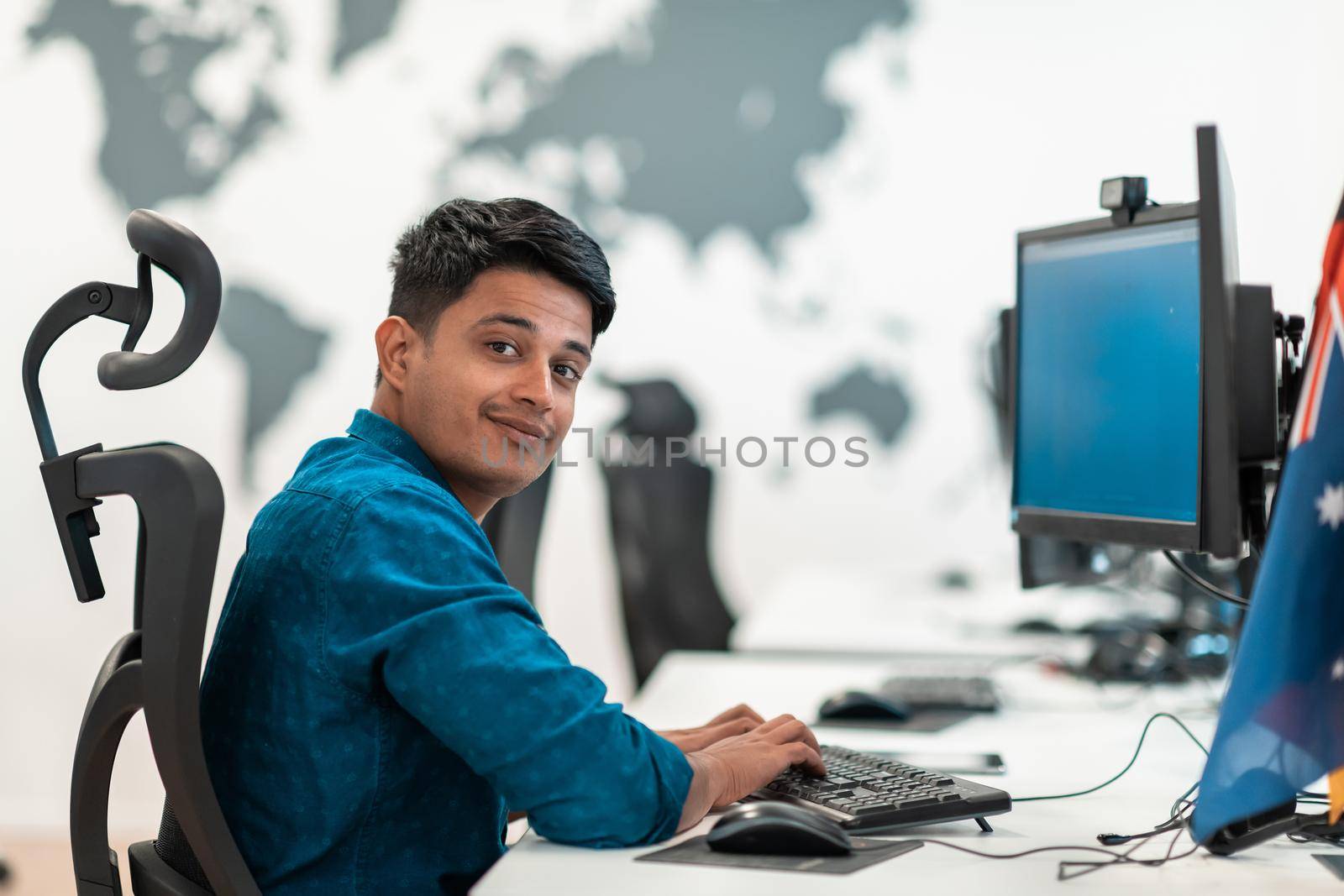 Casual businessman working on a desktop computer in modern open plan startup office interior. Selective focus. High-quality photo