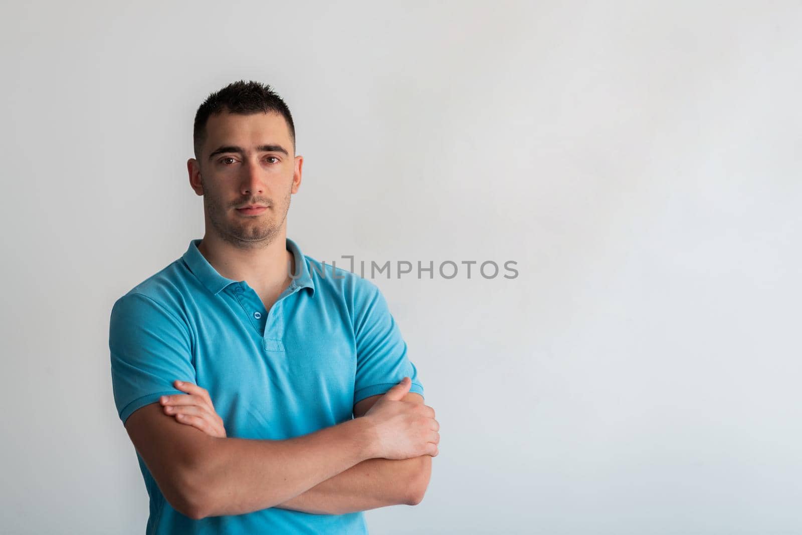 Formal business male portrait. A confident successful casual businessman or manager stands in front of a white background, arms crossed, looking directly at the camera and smiling friendly. High-quality photography.