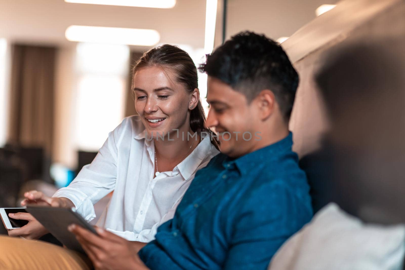 Multiethnic business people man with a female colleague working together on tablet computer in relaxation area of modern startup office. High-quality photo