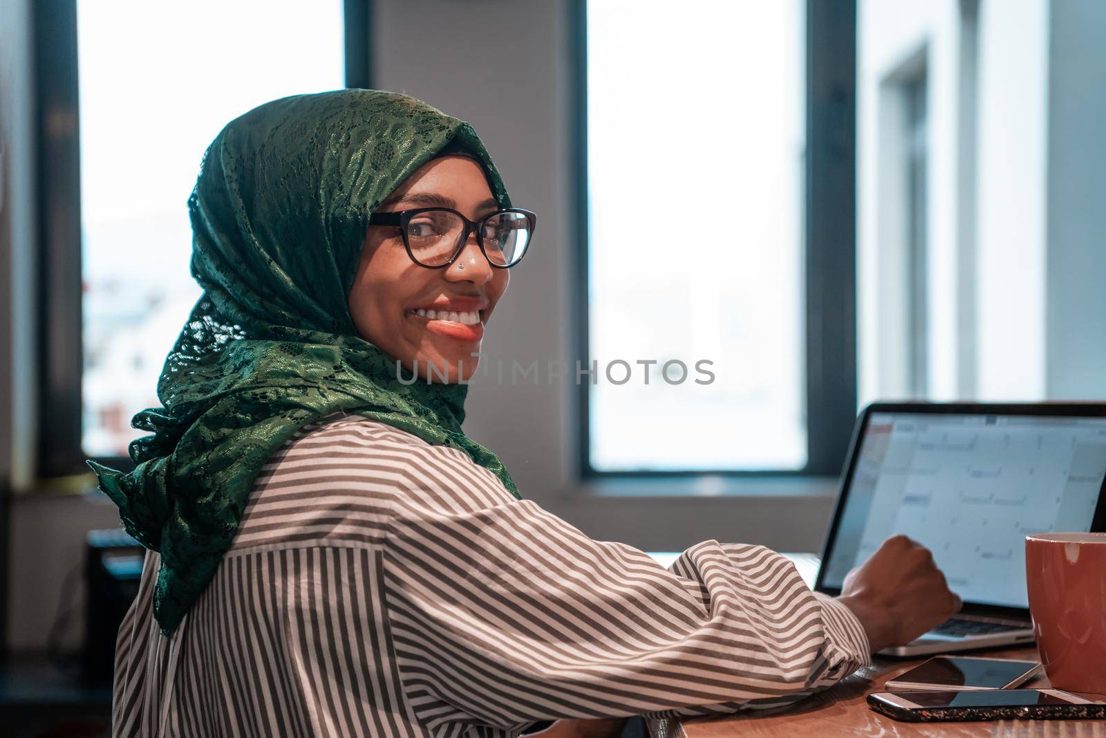 Businesswoman wearing a green hijab using laptop in relaxation area at modern open plan startup office. Selective focus. High-quality photo