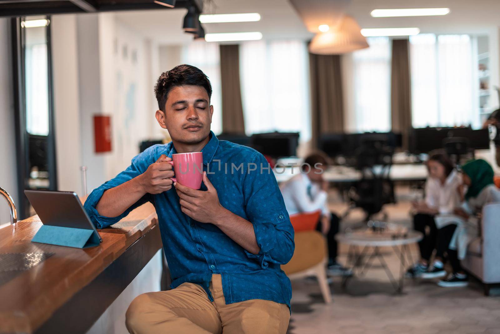 Casual businessman taking a break from the work using a laptop while drinking tea in relaxation area of modern open plan startup office. High-quality photo