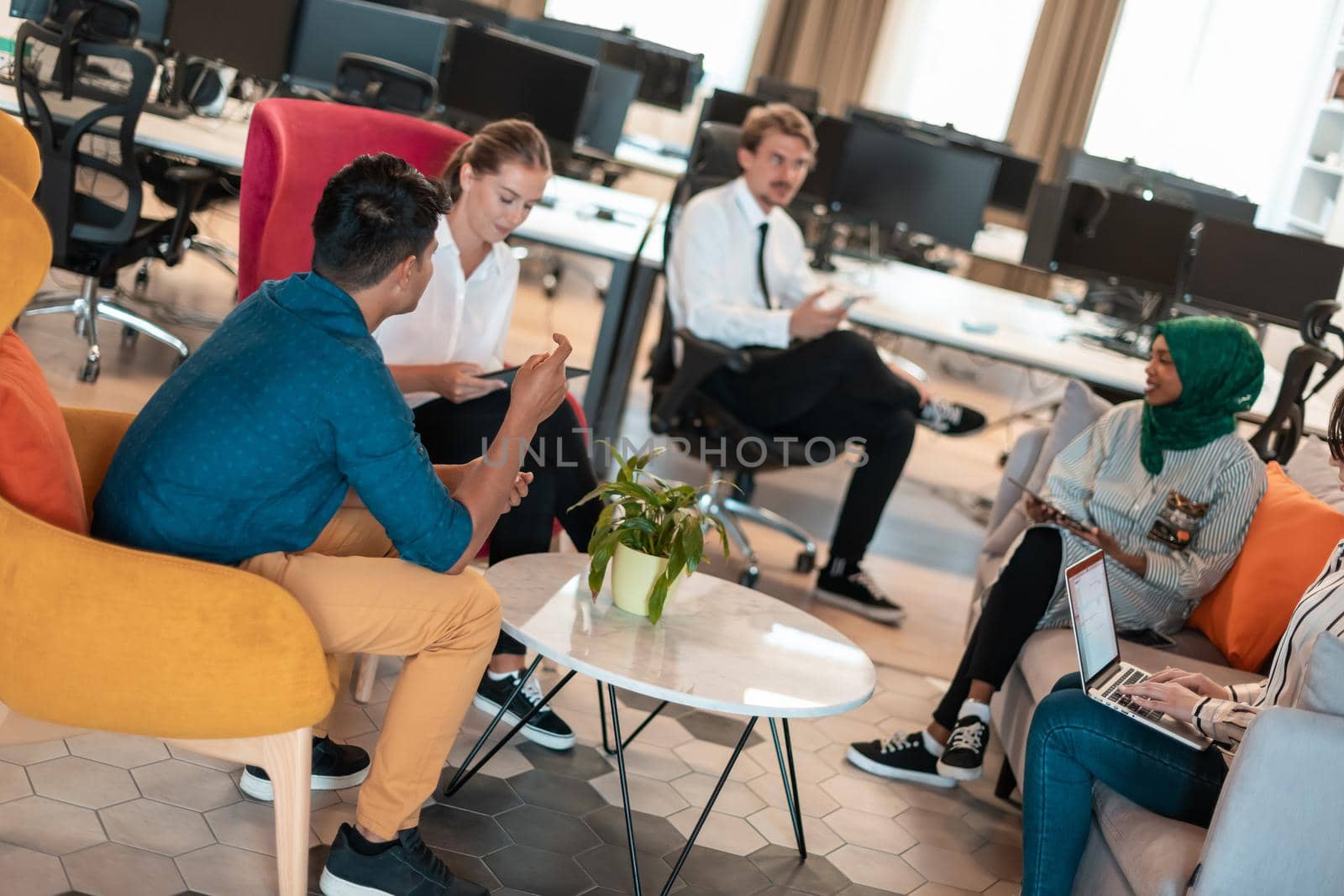 Multiethnic startup business team having brainstorming in relaxation area of modern office interior working on laptop and tablet computer. High-quality photo