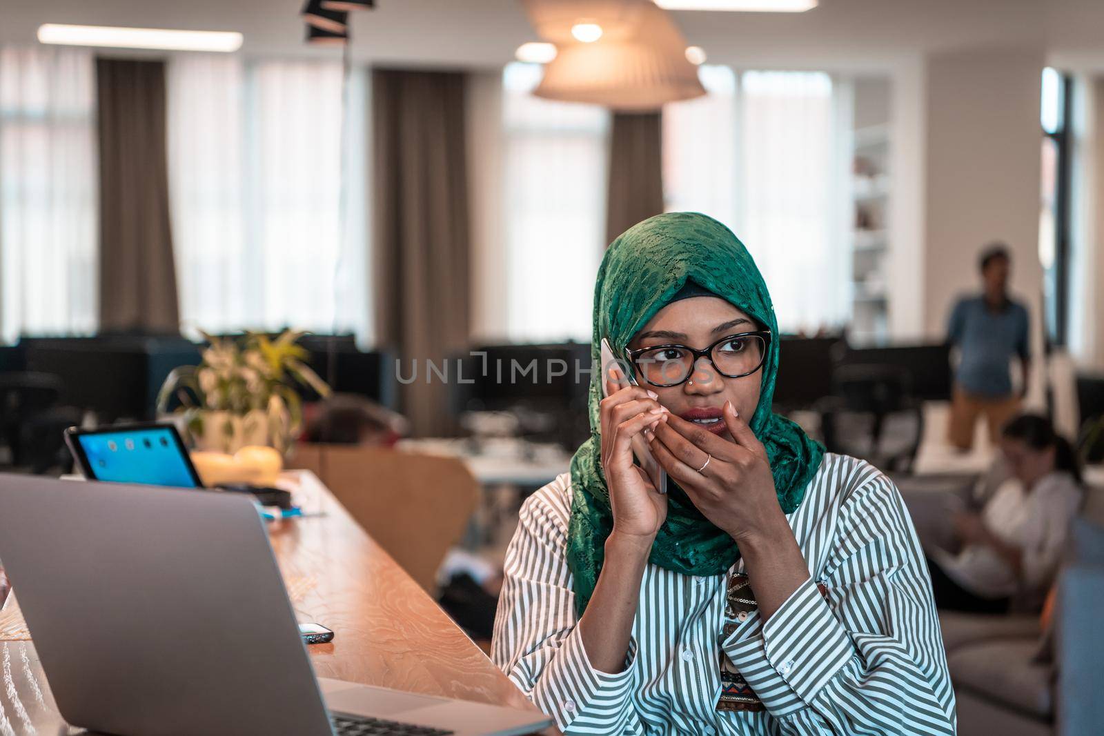 Smiling young woman talk on smartphone work on laptop look in distance thinking. Happy African American customer client using modern gadgets cellphone and computer at the home office. High-quality photo