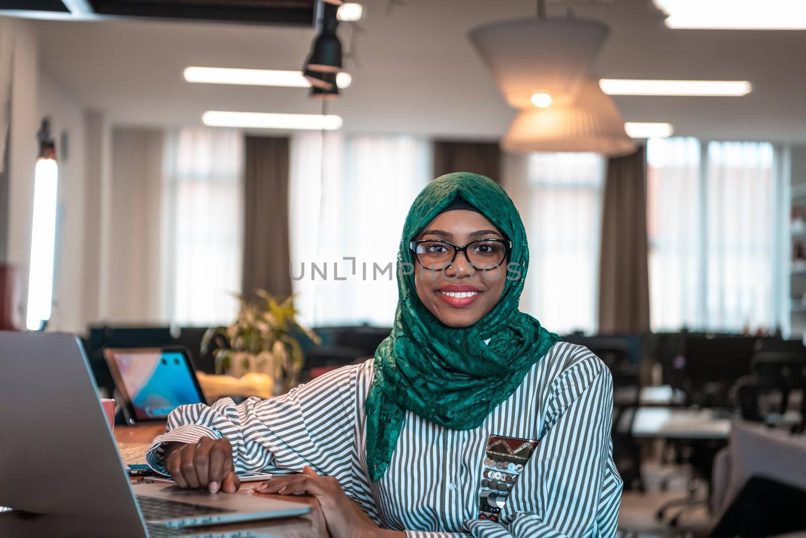 Businesswoman wearing a green hijab using laptop in relaxation area at modern open plan startup office. Selective focus. High-quality photo