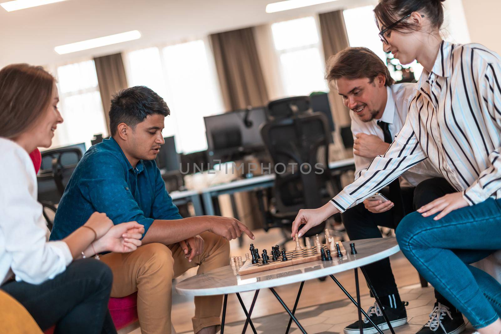 Multiethnic group of businesspeople playing chess while having a break in relaxation area at modern startup office. High-quality photo