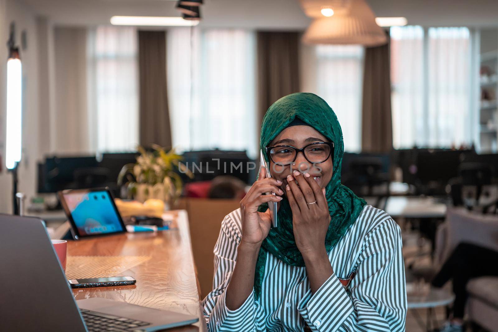 Smiling young woman talk on smartphone work on laptop look in distance thinking. Happy African American customer client use modern gadgets cellphone and computer at home office. by dotshock