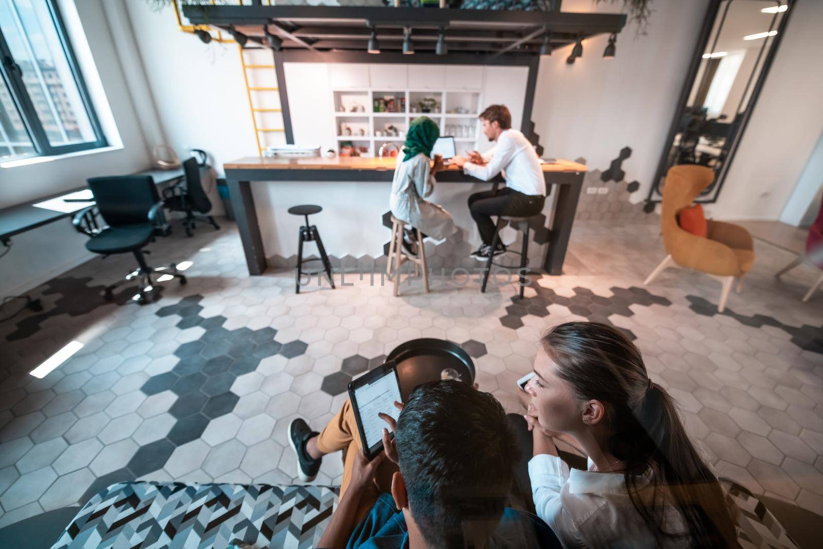 Group of casual multiethnic businesspeople taking a break from the work doing different things while enjoying free time in relaxation area at modern open plan startup office. High-quality photo