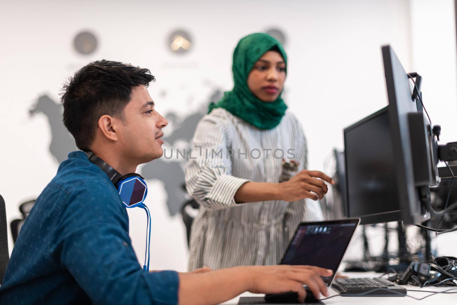 Multiethnic startup business team Arabian woman wearing a hijab on meeting in modern open plan office interior brainstorming, working on laptop and desktop computer. Selective focus. High-quality photo