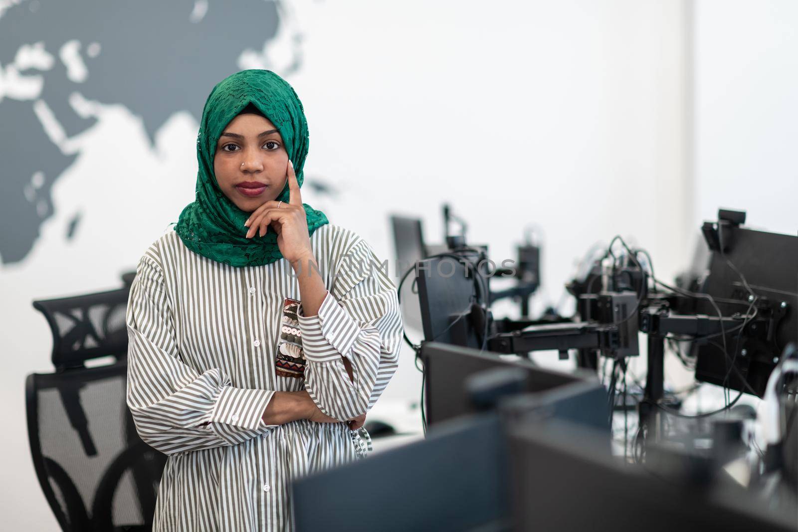 Portrait of muslim black female software developer with green hijab standing at modern open plan startup office. Selective focus by dotshock