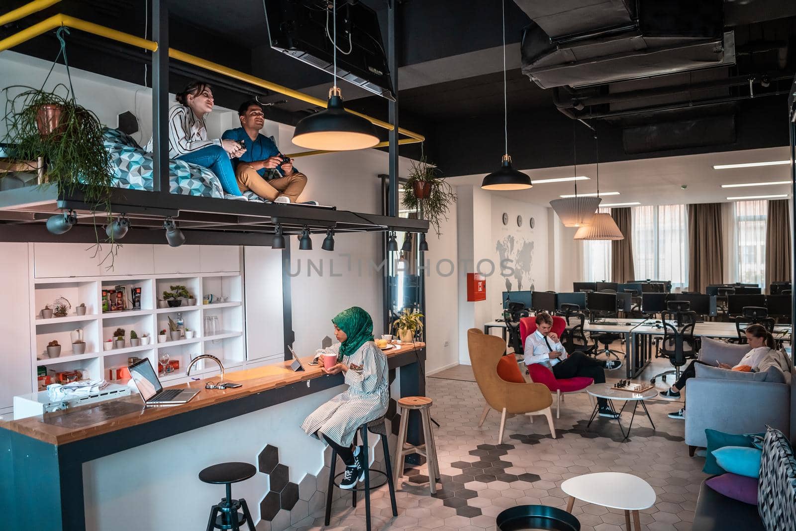 Group of casual multiethnic businesspeople taking a break from the work doing different things while enjoying free time in relaxation area at modern open plan startup office. High-quality photo