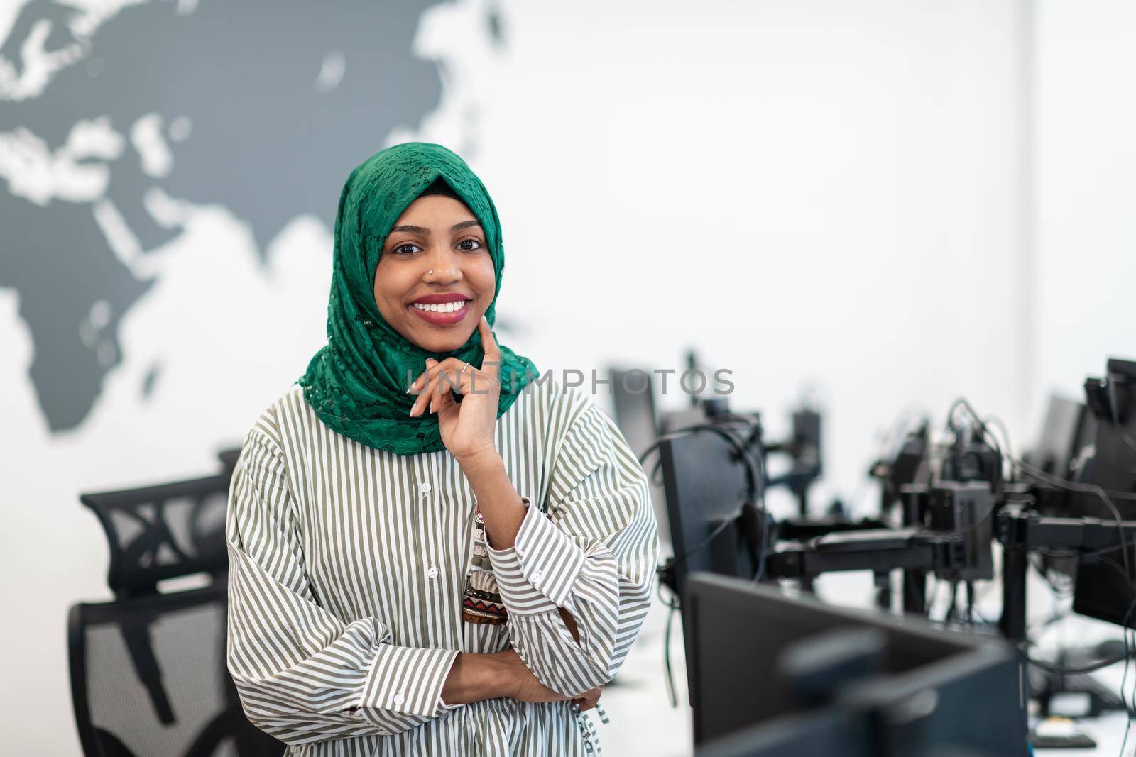 Portrait of Muslim black female software developer with green hijab standing at modern open plan startup office. Selective focus. High-quality photo