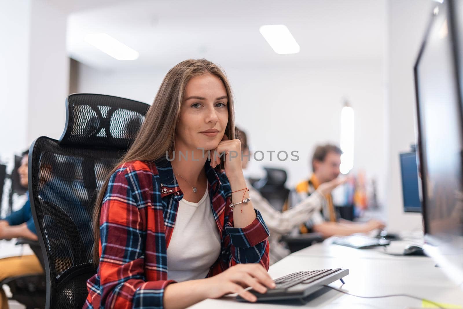 Casual businesswoman working on a desktop computer in modern open plan startup office interior. Selective focus. High-quality photo