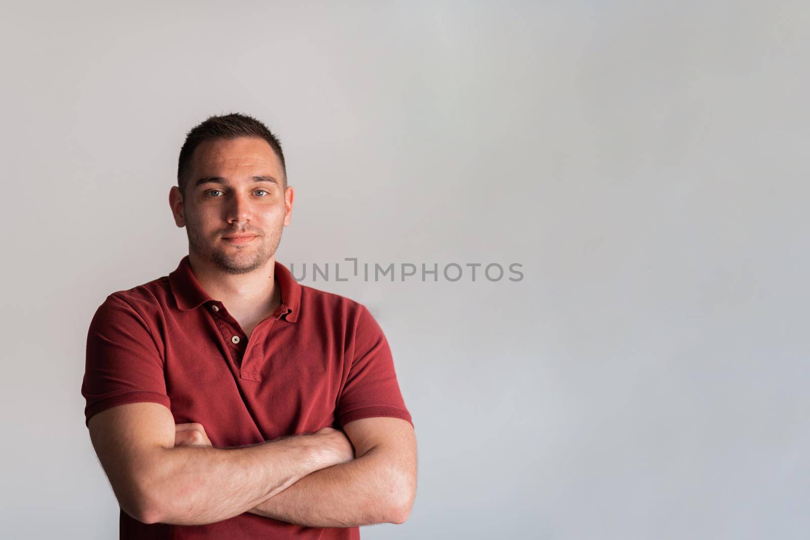 Formal business male portrait. A confident successful casual businessman or manager stands in front of a white background, arms crossed, looking directly at the camera and smiling friendly. High quality photography by dotshock