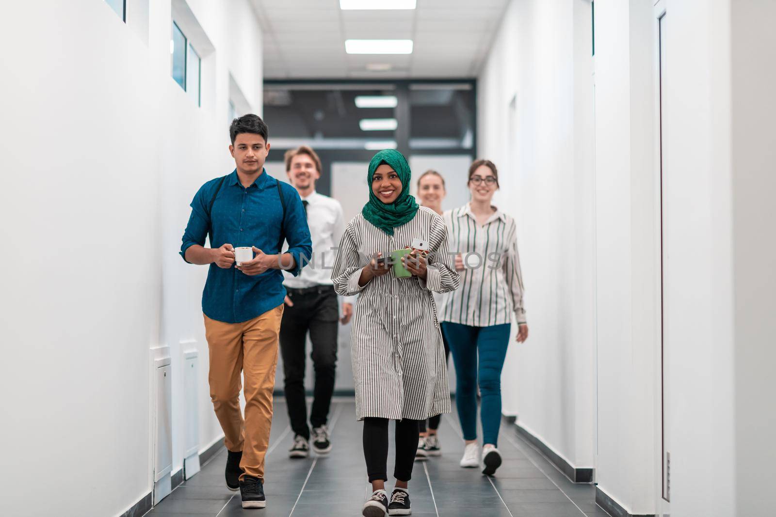 Multi-ethnic startup business team walking through the hallway of the building while coming back from a coffee break. High-quality photo