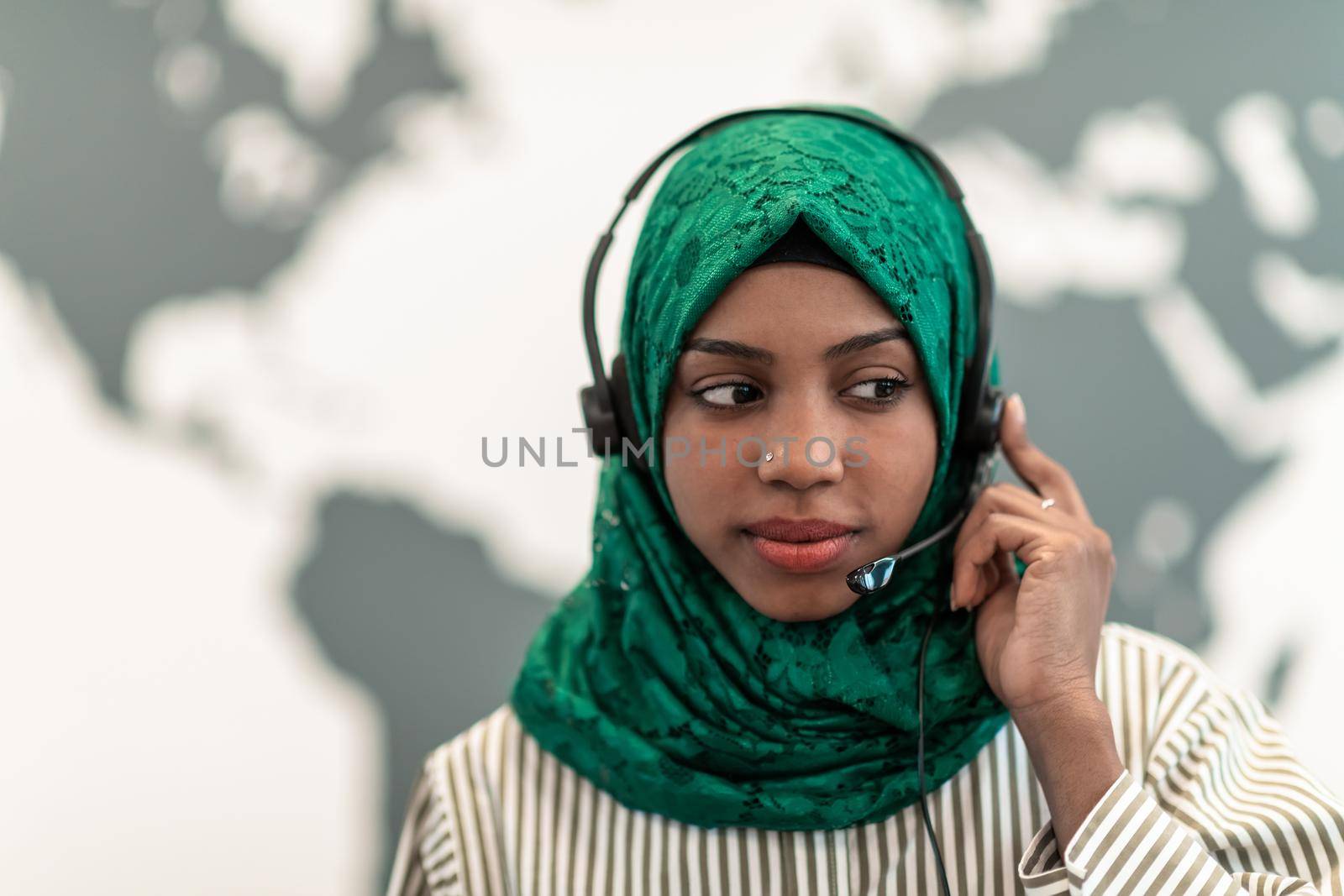 Afro Muslim female with green hijab scarf customer representative businesswoman with phone headset helping and supporting online with the customer in a modern call center. High-quality photo