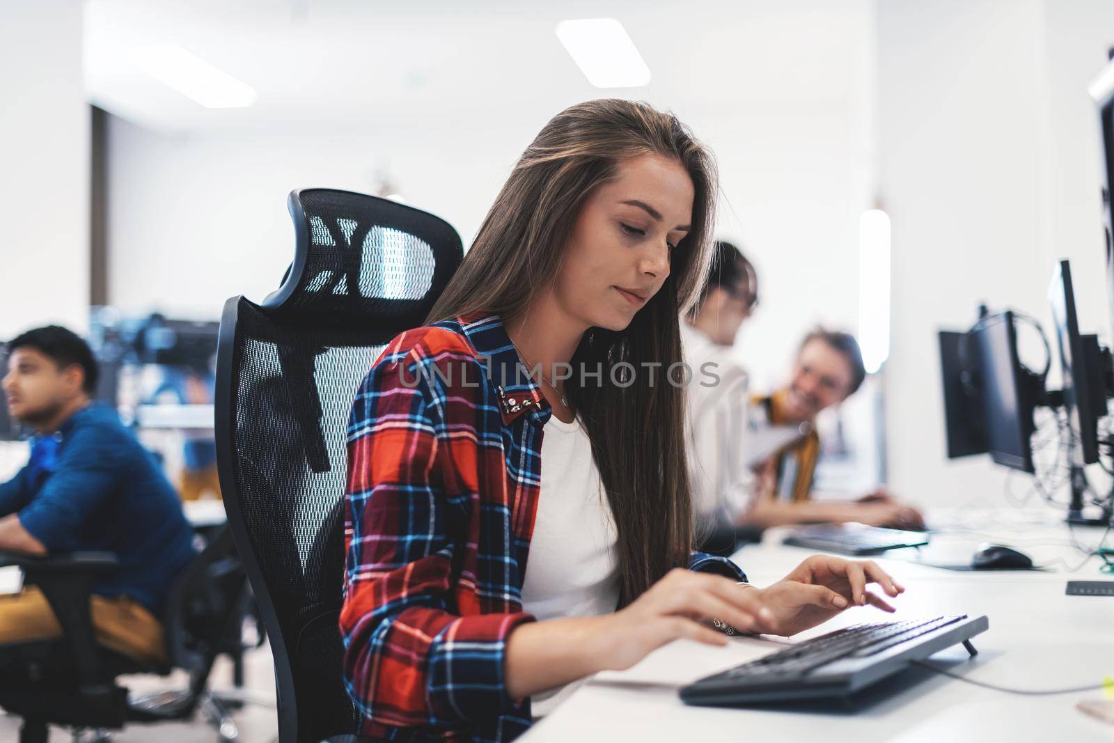 Casual business woman working on desktop computer in modern open plan startup office interior. Selective focus by dotshock