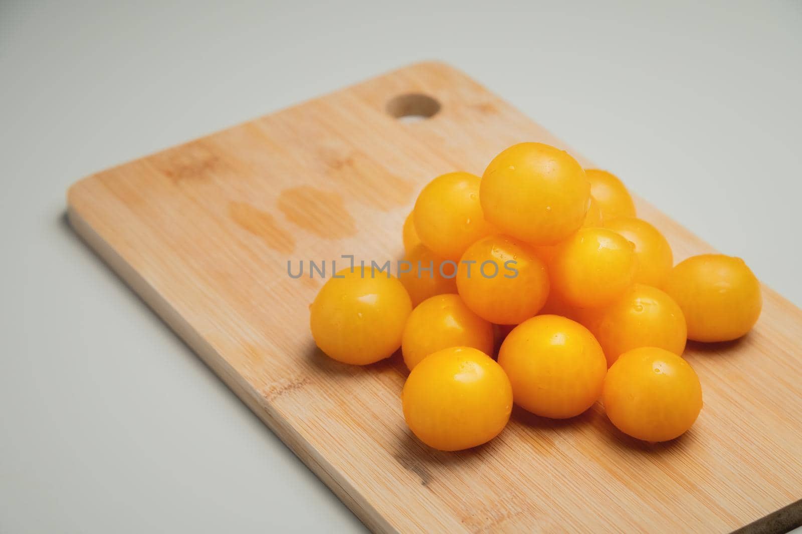 A heap of yellow cherry tomatoes on a wooden cutting board in the kitchen on a white table by yanik88
