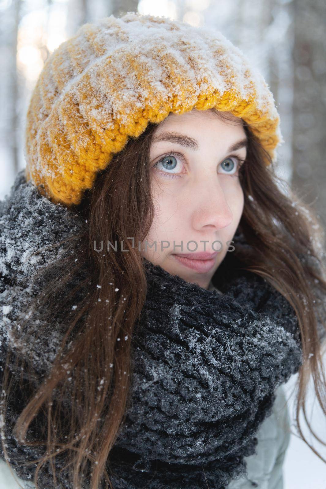 portrait of a smiling young caucasian woman in a bright woolen hat and scarf, against the backdrop of a snowy forest