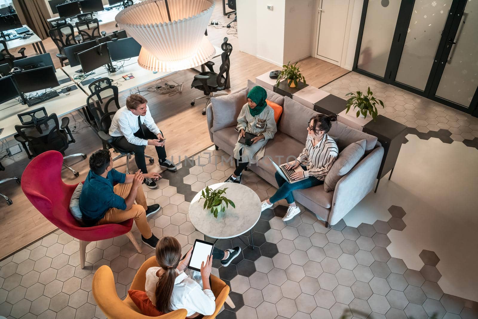 Top view photo of Multiethnic startup business team having brainstorming in relaxation area of modern office interior working on laptop and tablet computer. High-quality photo