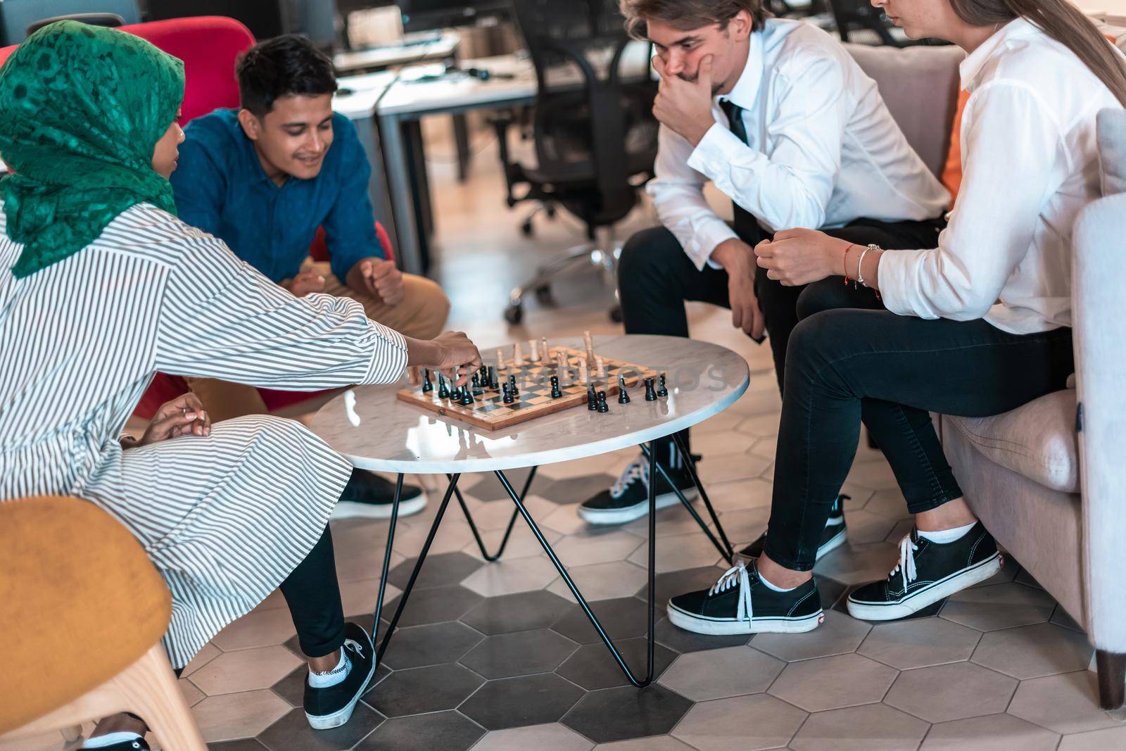 Multiethnic group of business people playing chess while having a break in relaxation area at modern startup office by dotshock