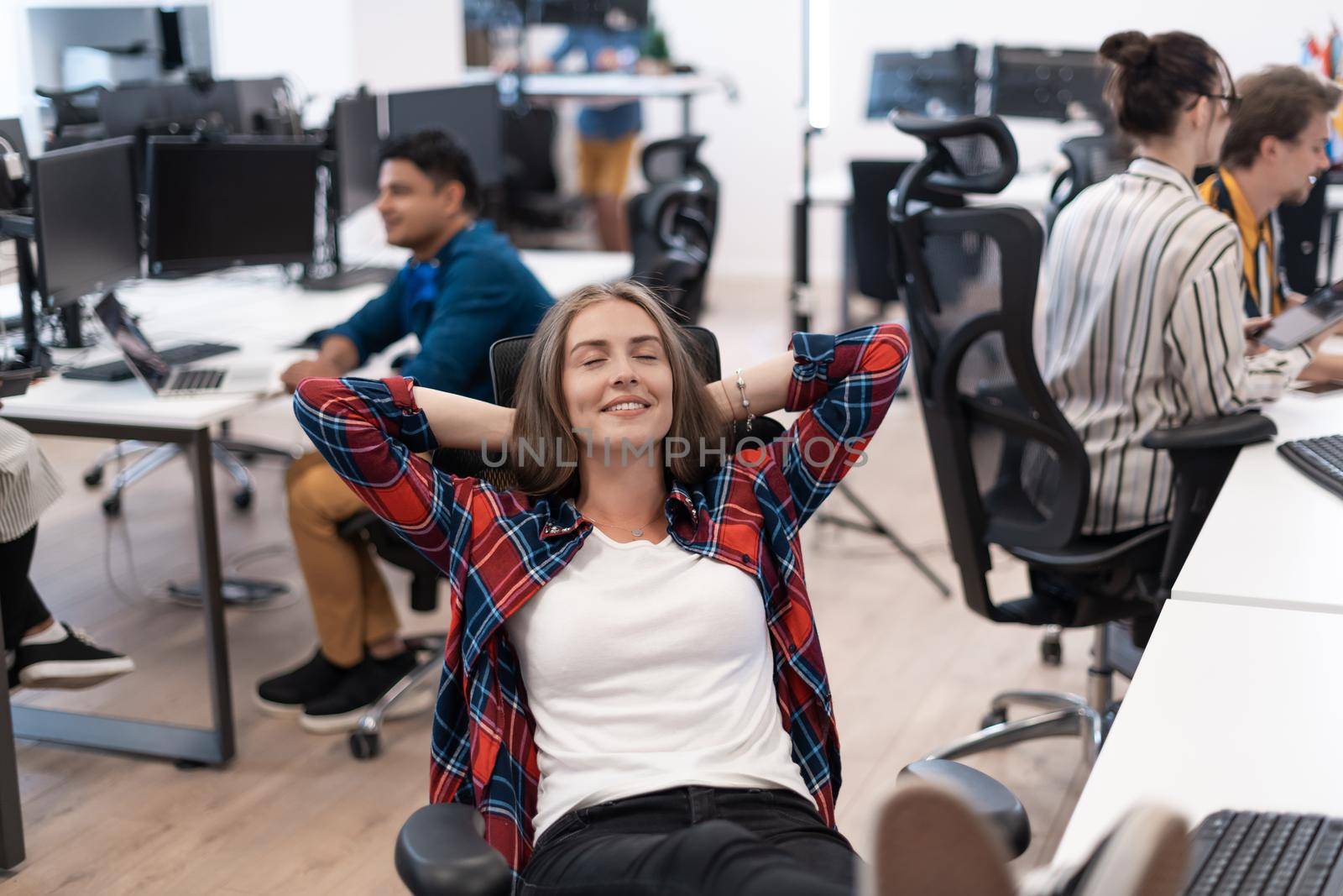 Casual business woman taking a break with legs on her table while working on desktop computer in modern open plan startup office interior. Selective focus by dotshock