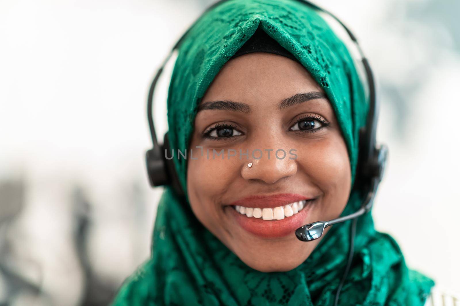 Afro Muslim female with green hijab scarf customer representative businesswoman with phone headset helping and supporting online with the customer in a modern call center. High-quality photo