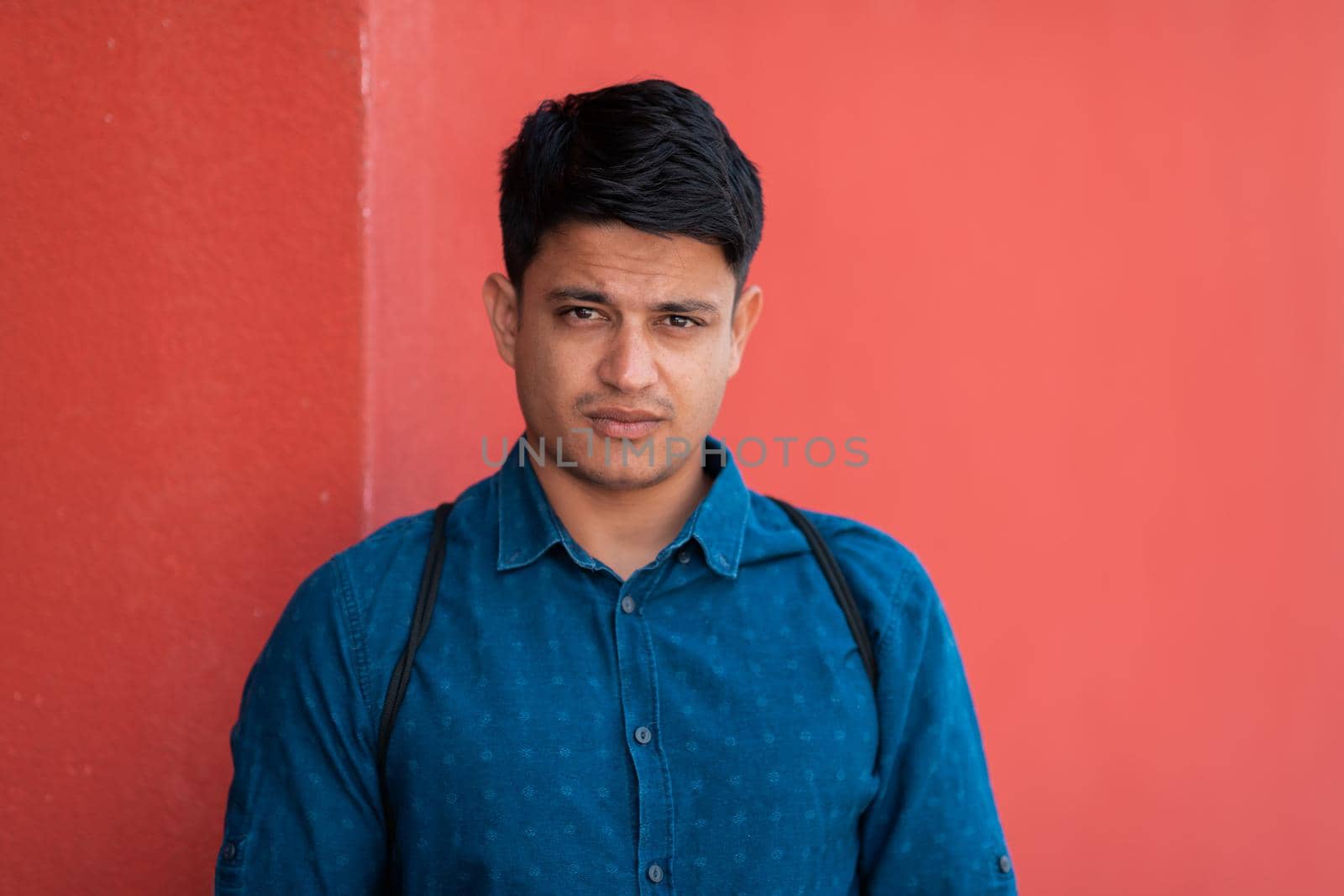 Startup business portrait of casual businessman with a blue shirt and backpack in front of a red wall. High-quality photo