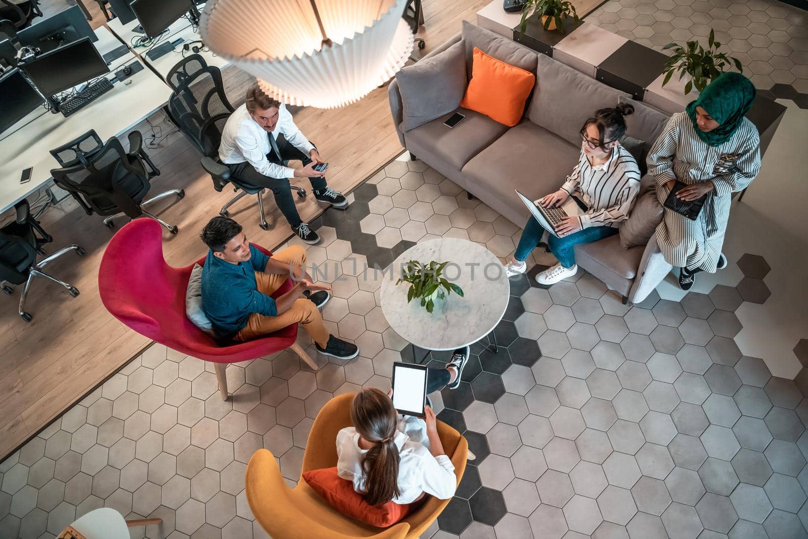 Top view photo of Multiethnic startup business team having brainstorming in relaxation area of modern office interior working on laptop and tablet computer by dotshock