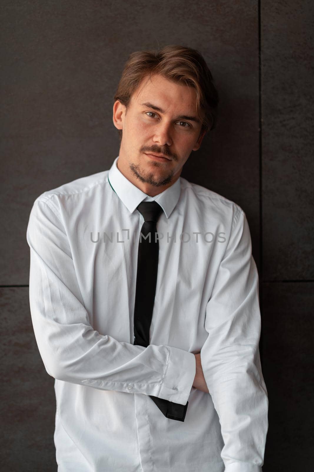 Portrait of startup businessman in a white shirt with a black tie standing in front of the gray wall outside. High-quality photo