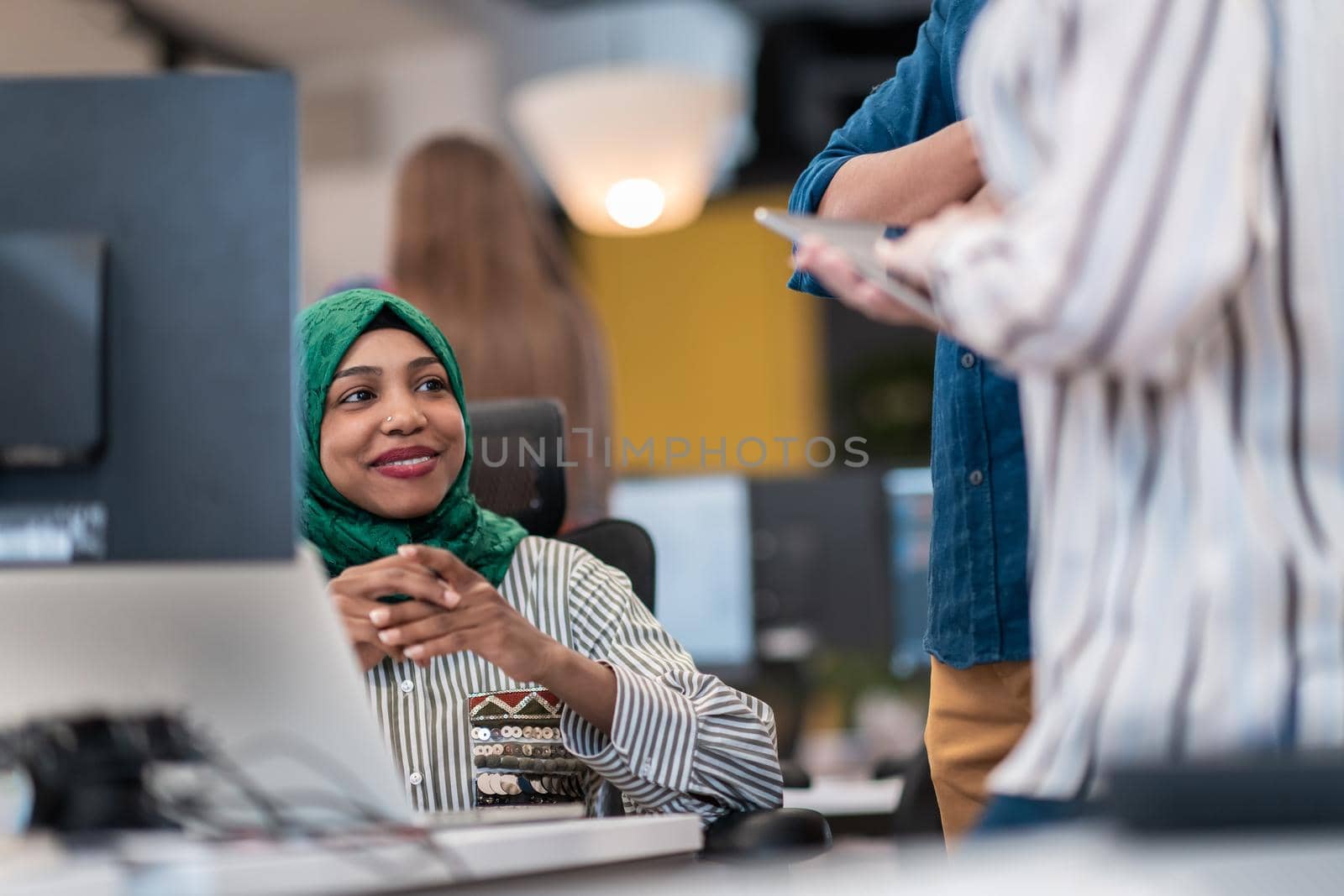 Multiethnic startup business team Arabian woman wearing a hijab on meeting in modern open plan office interior brainstorming, working on laptop and desktop computer. Selective focus by dotshock