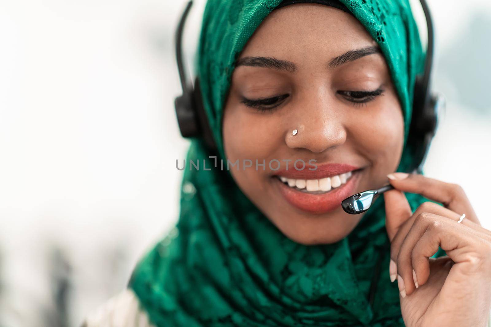 Afro Muslim female with green hijab scarf customer representative businesswoman with phone headset helping and supporting online with the customer in a modern call center. High-quality photo