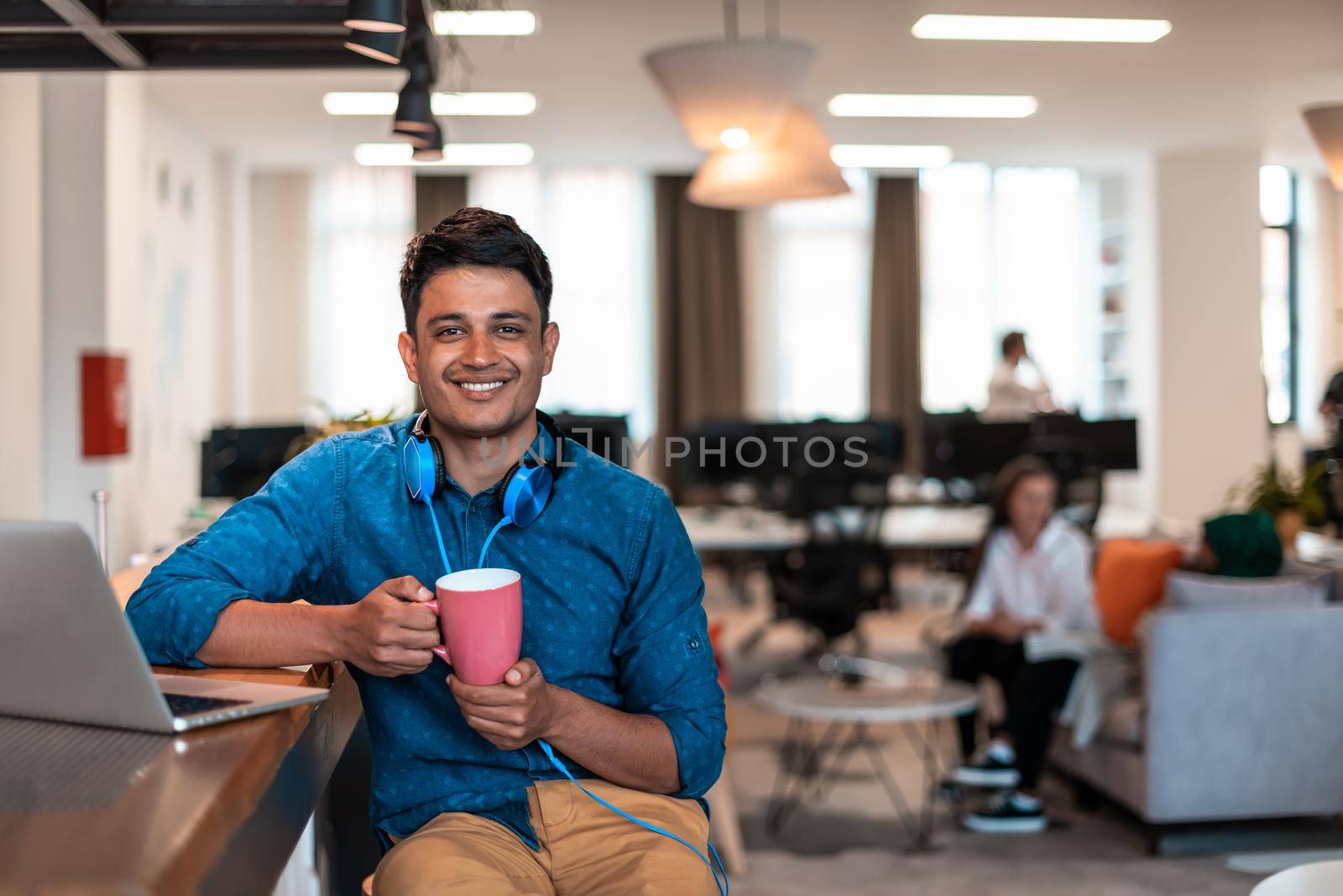 Casual business man taking break from the work using laptop while drinking tea in relaxation area of modern open plan startup office by dotshock