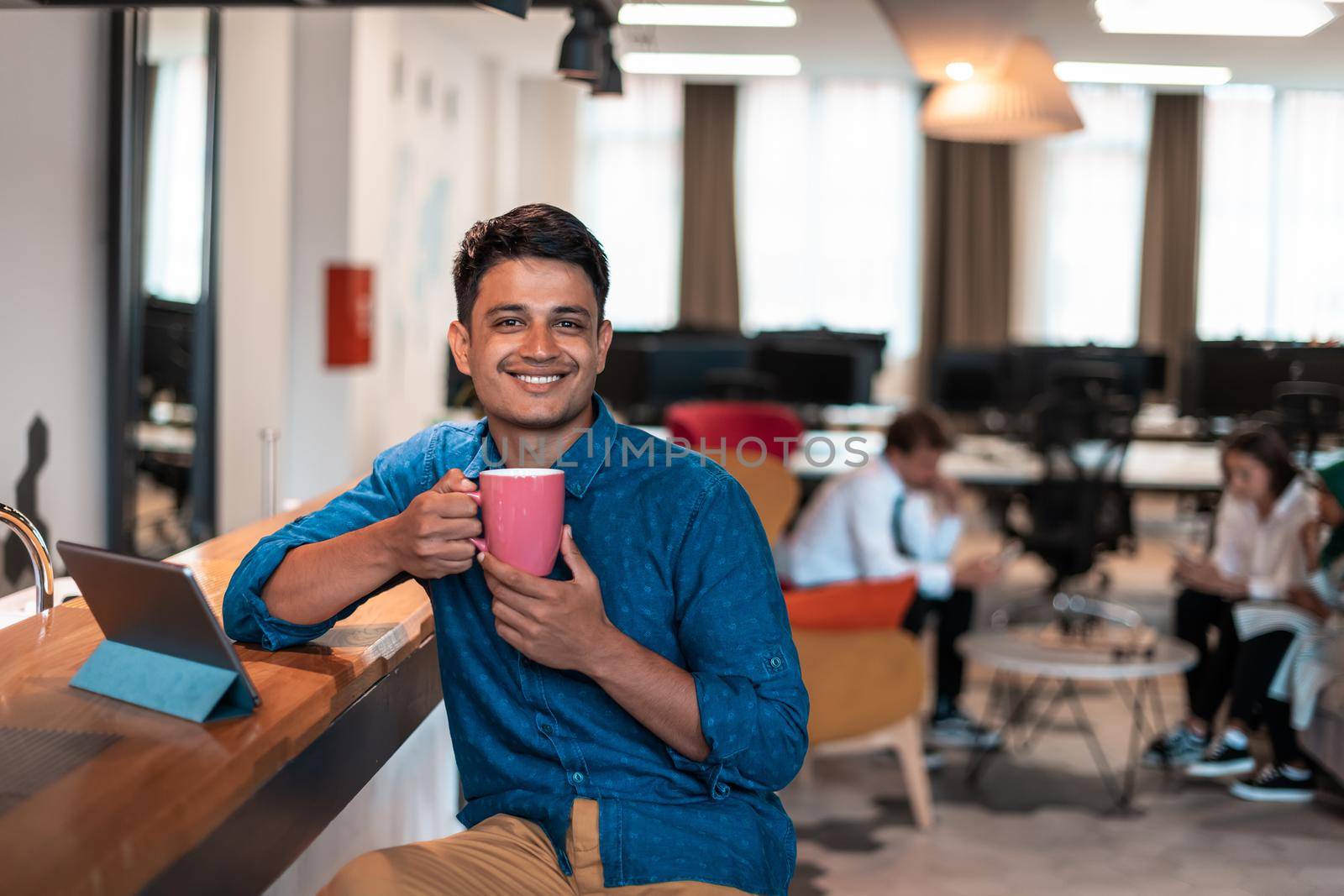 Casual businessman taking a break from the work using a laptop while drinking tea in relaxation area of modern open plan startup office. High-quality photo