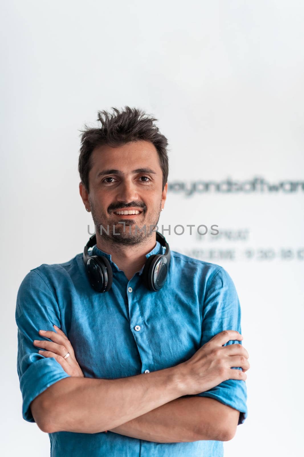 Formal business male portrait. A confident successful casual businessman or manager stands in front of a white background, arms crossed, looking directly at the camera and smiling friendly. High quality photography by dotshock