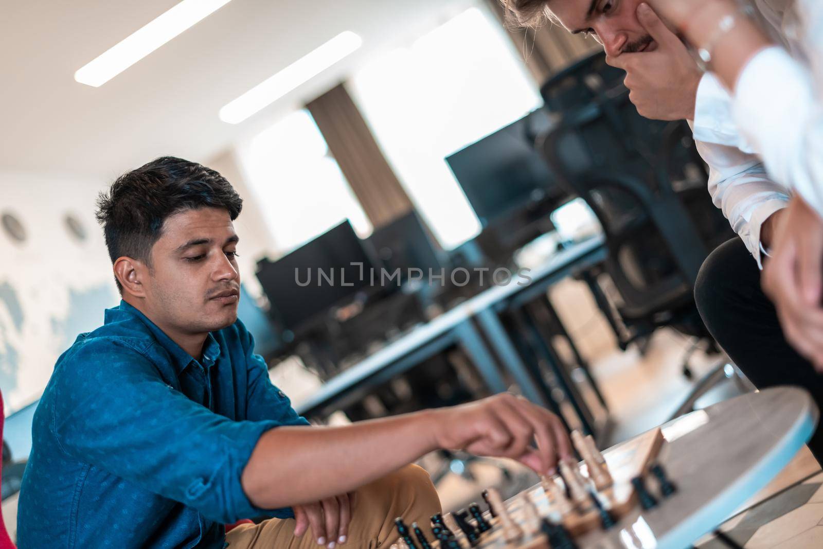 Multiethnic group of business people playing chess while having a break in relaxation area at modern startup office by dotshock