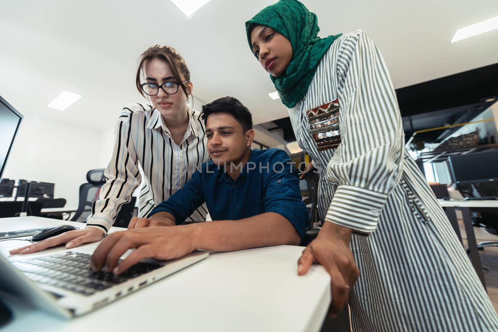 Multiethnic startup business team Arabian woman wearing a hijab on meeting in modern open plan office interior brainstorming, working on laptop and desktop computer. Selective focus. High-quality photo