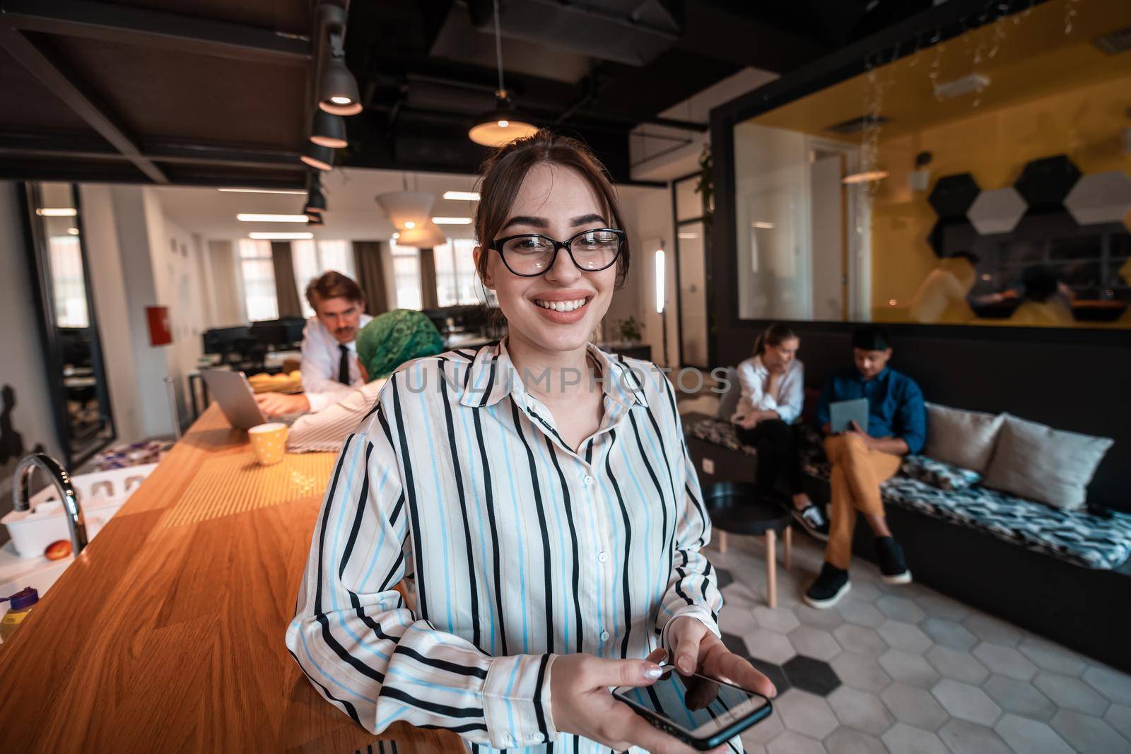 Businesswoman with glasses using a smartphone at modern startup open plan office interior. Selective focus. High-quality photo