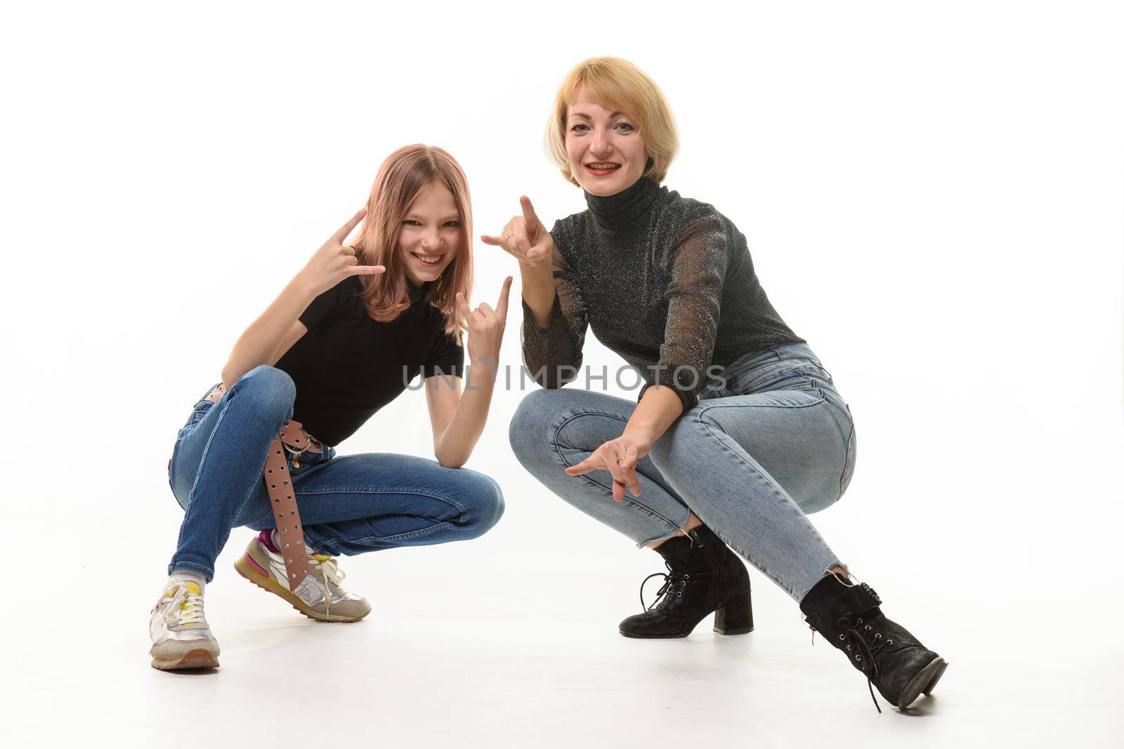 Mother and daughter teenager knelt down and cheerfully show youth gestures in the frame a