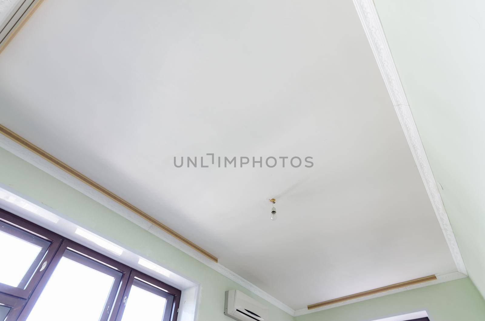 Plastered white ceiling in the room, a temporary light bulb hangs on the ceiling a