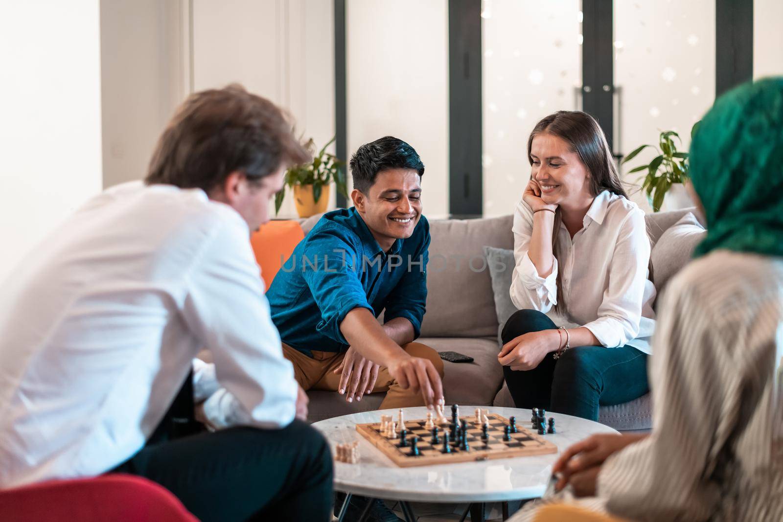 Multiethnic group of businesspeople playing chess while having a break in relaxation area at modern startup office. Selective focus. High-quality photo