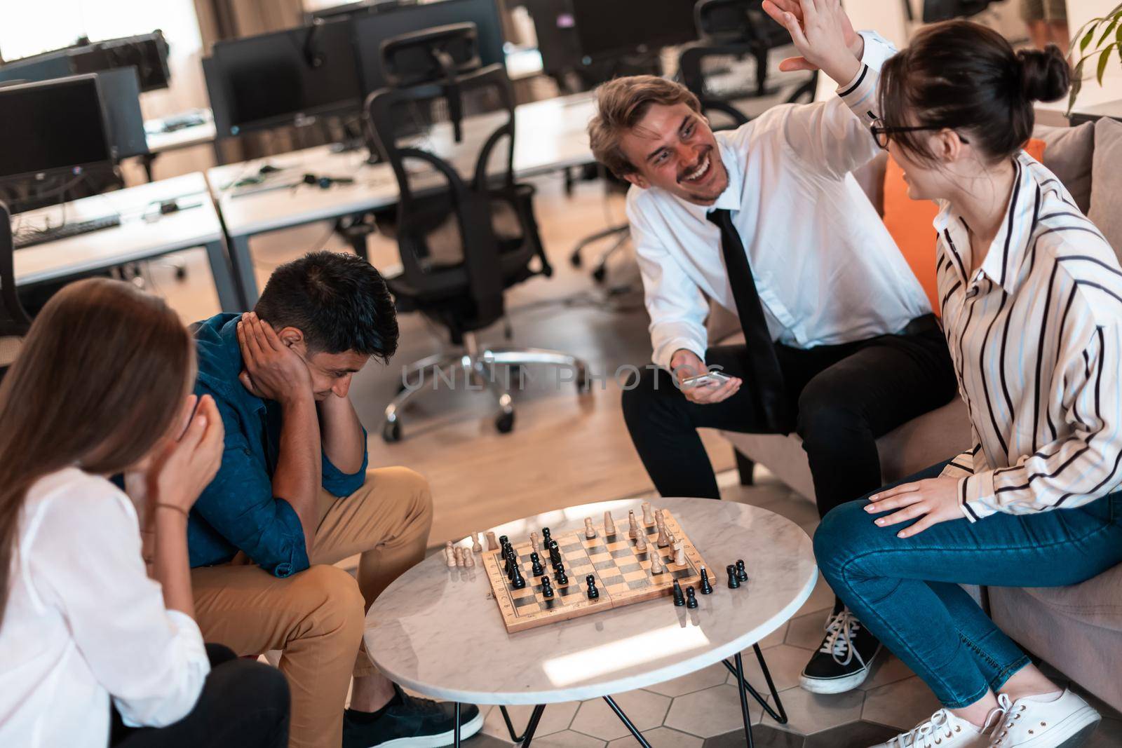 Multiethnic group of businesspeople playing chess while having a break in relaxation area at modern startup office. High-quality photo