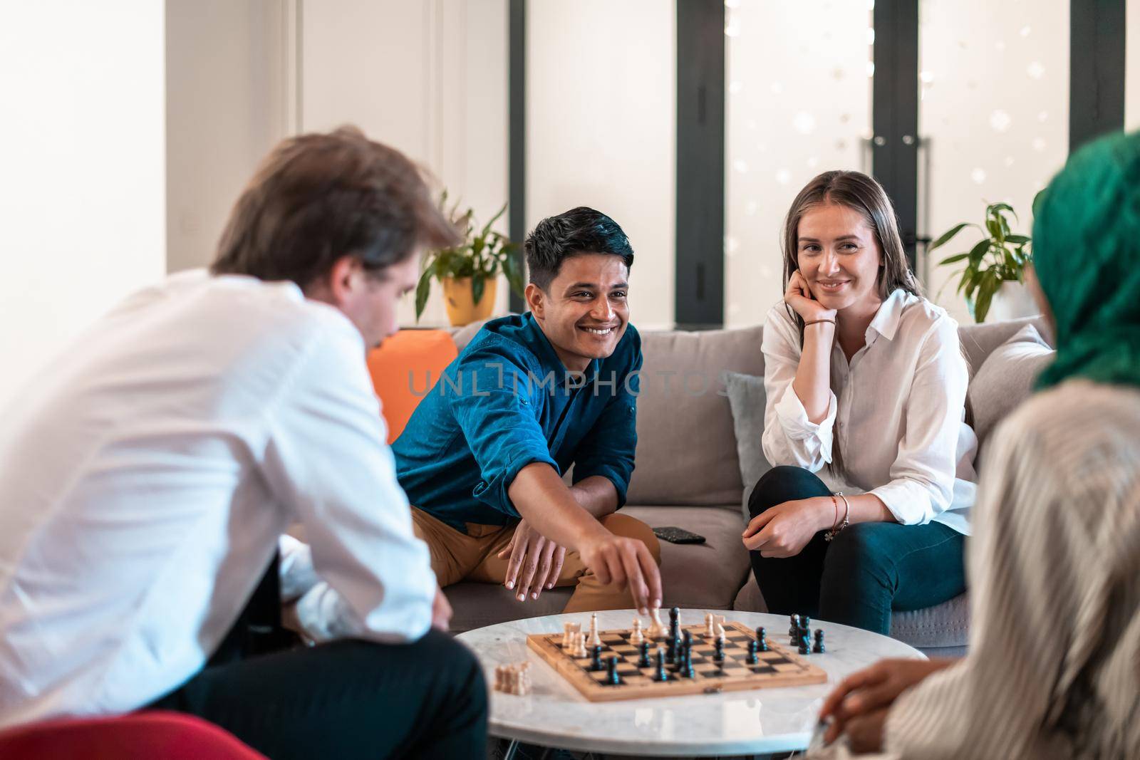 Multiethnic group of businesspeople playing chess while having a break in relaxation area at modern startup office. Selective focus. High-quality photo