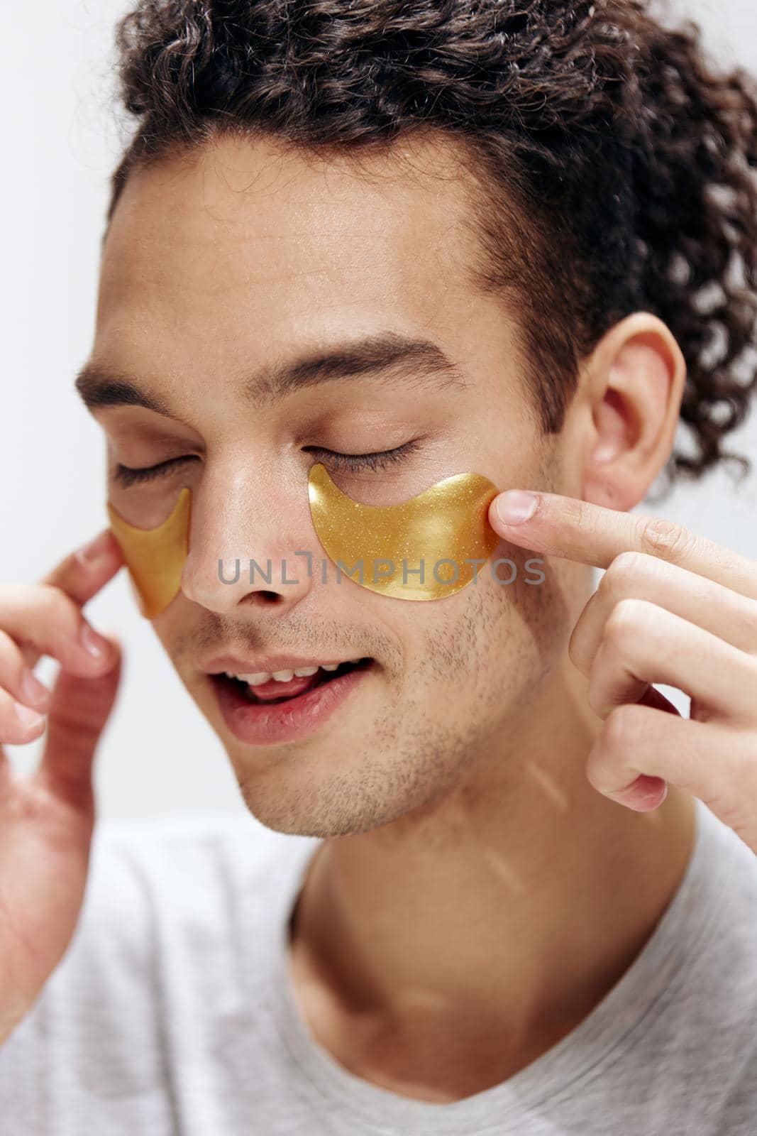 A young man with patches on the face touches face with hands light background. High quality photo