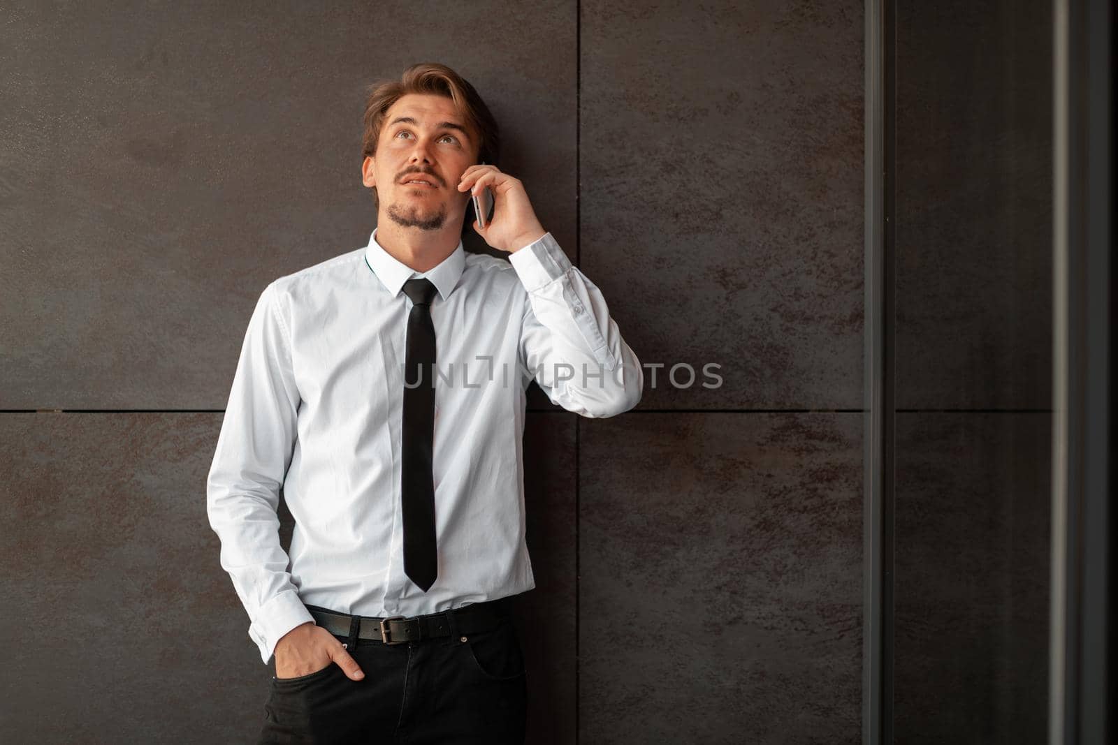 Startup businessman in a white shirt with a black tie using smartphone while standing in front of gray wall during a break from work outside. High-quality photo